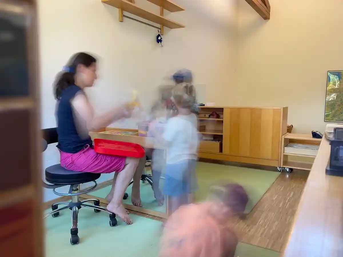 Eine Erziehering sitzt auf einem Drehstuhl und spricht mit Kindern im Kinderhaus St. Martin in Konstanz.