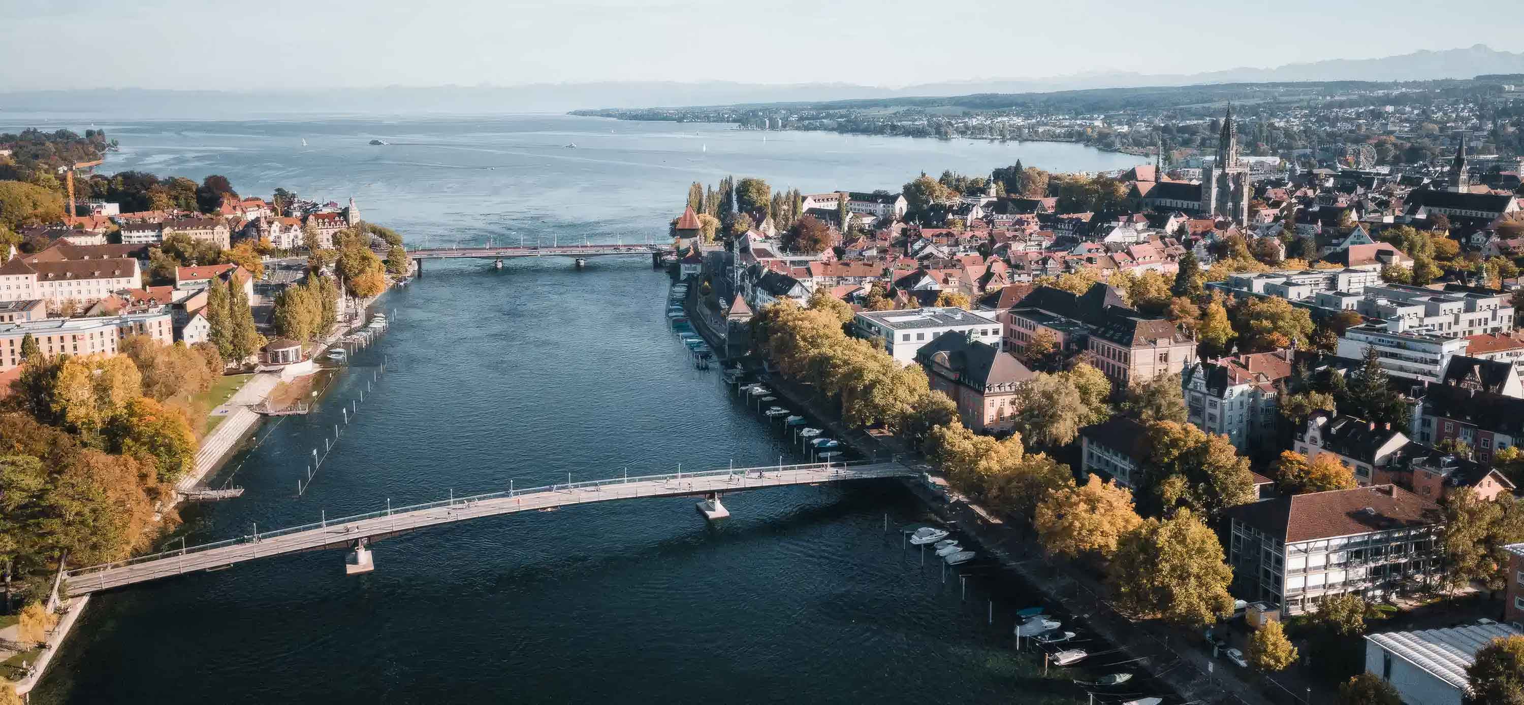 Luftaufnahme von Konstanz am Seerhein bei sonnigem Wetter mit Blick auf die Fahrradbrücke, die Rheinbrücke und den Übergang in den Bodensee, mit der Altstadt und dem Konstanzer Münster auf der rechten Seite. Bildrechte: Tourismus Konstanz.