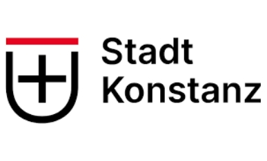 Das Logo besteht aus einem stilisierten Wappen auf der linken Seite und dem Schriftzug "Stadt Konstanz" auf der rechten Seite. Das Wappen ist u-förmig, mit einer roten horizontalen Linie oben und einem schwarzen Kreuz in der Mitte auf weißem Grund. Der Schriftzug ist in schwarzer, serifenloser Schrift in zwei Zeilen gesetzt: "Stadt" oben und "Konstanz" unten. Das Logo ist insgesamt schlicht und modern gehalten.